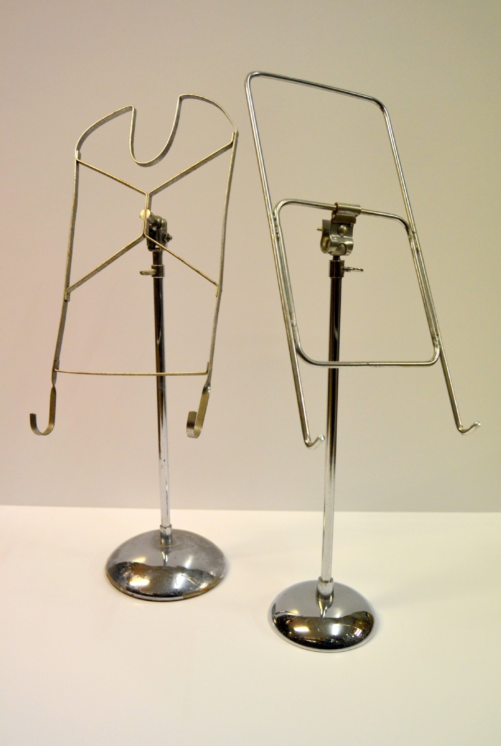 A pair of adjustable silver chrome shirt display stands featuring circular domed bases and custom wireframes with hooks.