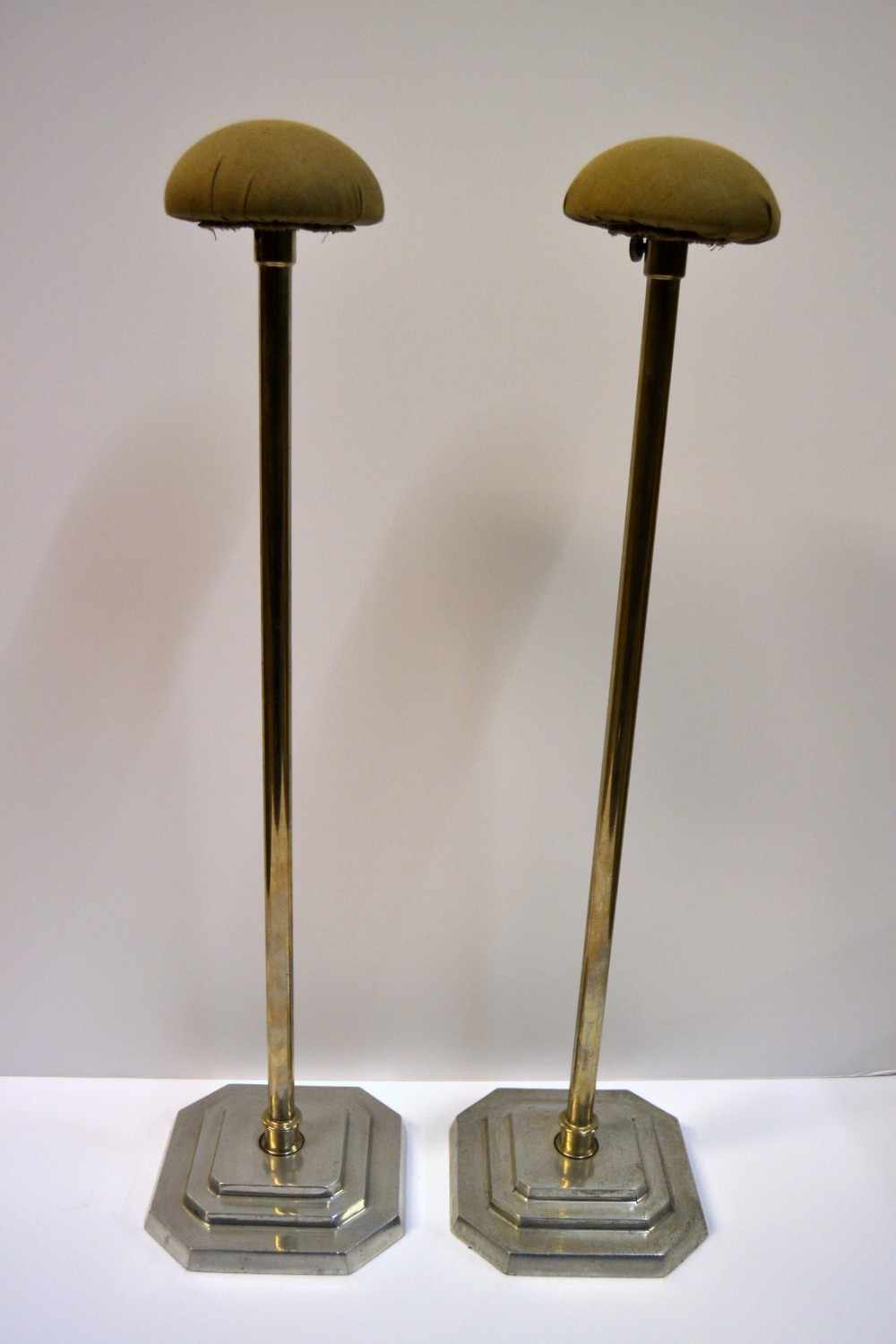 A pair of 1930s Art Deco hat stands featuring stepped metallic bases, slim upright pillars, and olive green fabric-padded domes.