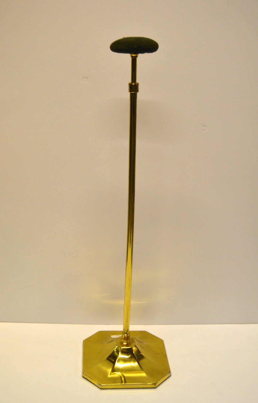 An adjustable brass hat stand featuring an octagonal stepped base, telescopic central stem, and dark fabric padded top.