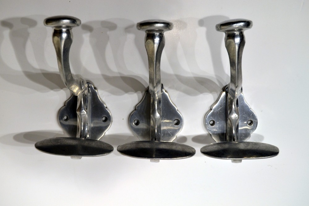 A set of three polished cast aluminium wall-mounted coat and hat hooks featuring shaped backplates and curved pegs.