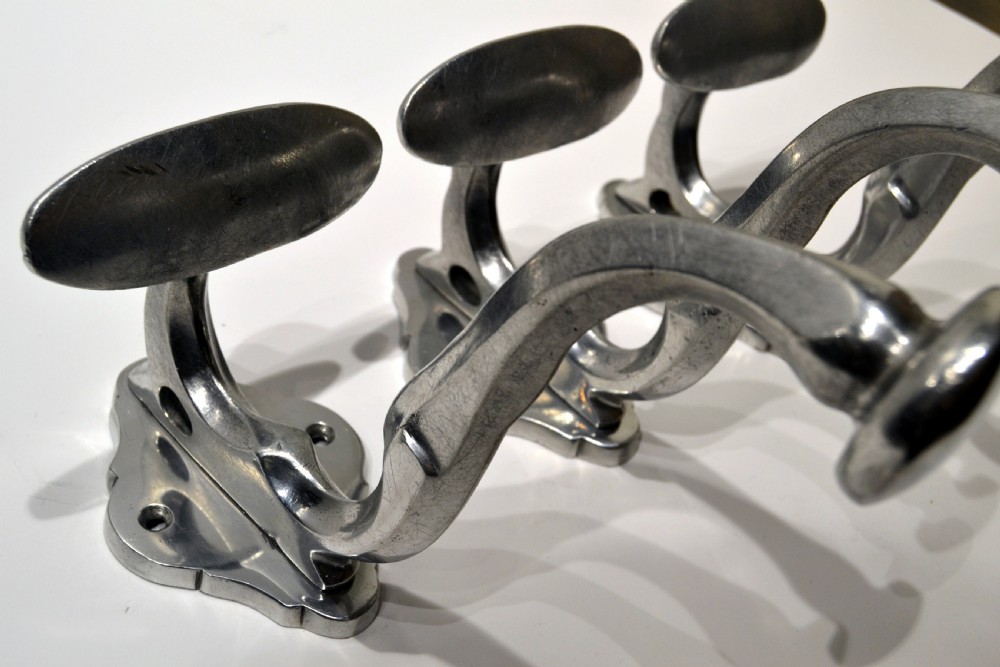 A set of three polished cast aluminium wall-mounted coat and hat hooks featuring shaped backplates and curved pegs. View II