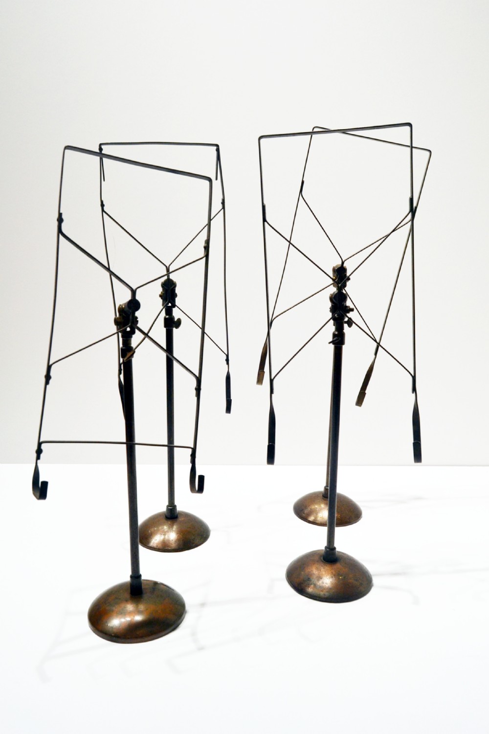 A set of four vintage 1930s adjustable metal shirt stands with circular weighted bases and geometric wire display frames.
