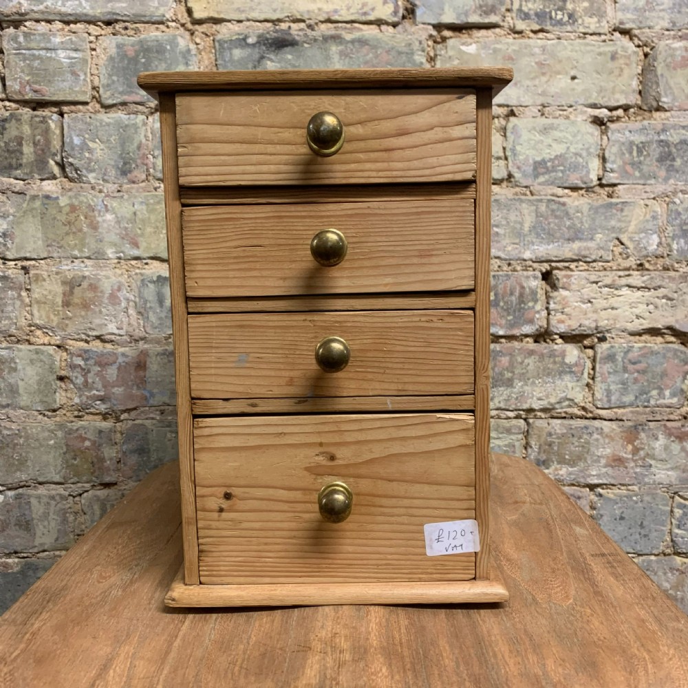 A small tabletop pine cabinet with four stacked drawers, each fitted with a round brass knob.