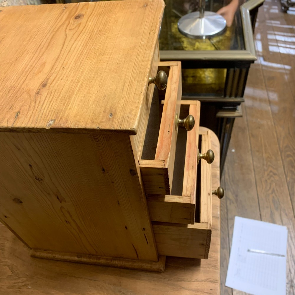 A small tabletop pine cabinet with four stacked drawers, each fitted with a round brass knob. View IV