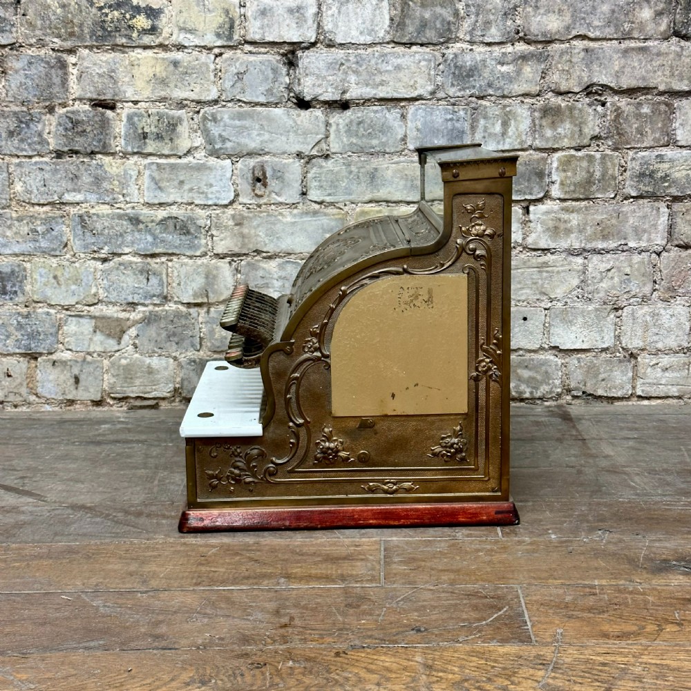 An ornate antique brass National cash register featuring a marble shelf, glass indicator top, and detailed relief scrolls. View VI
