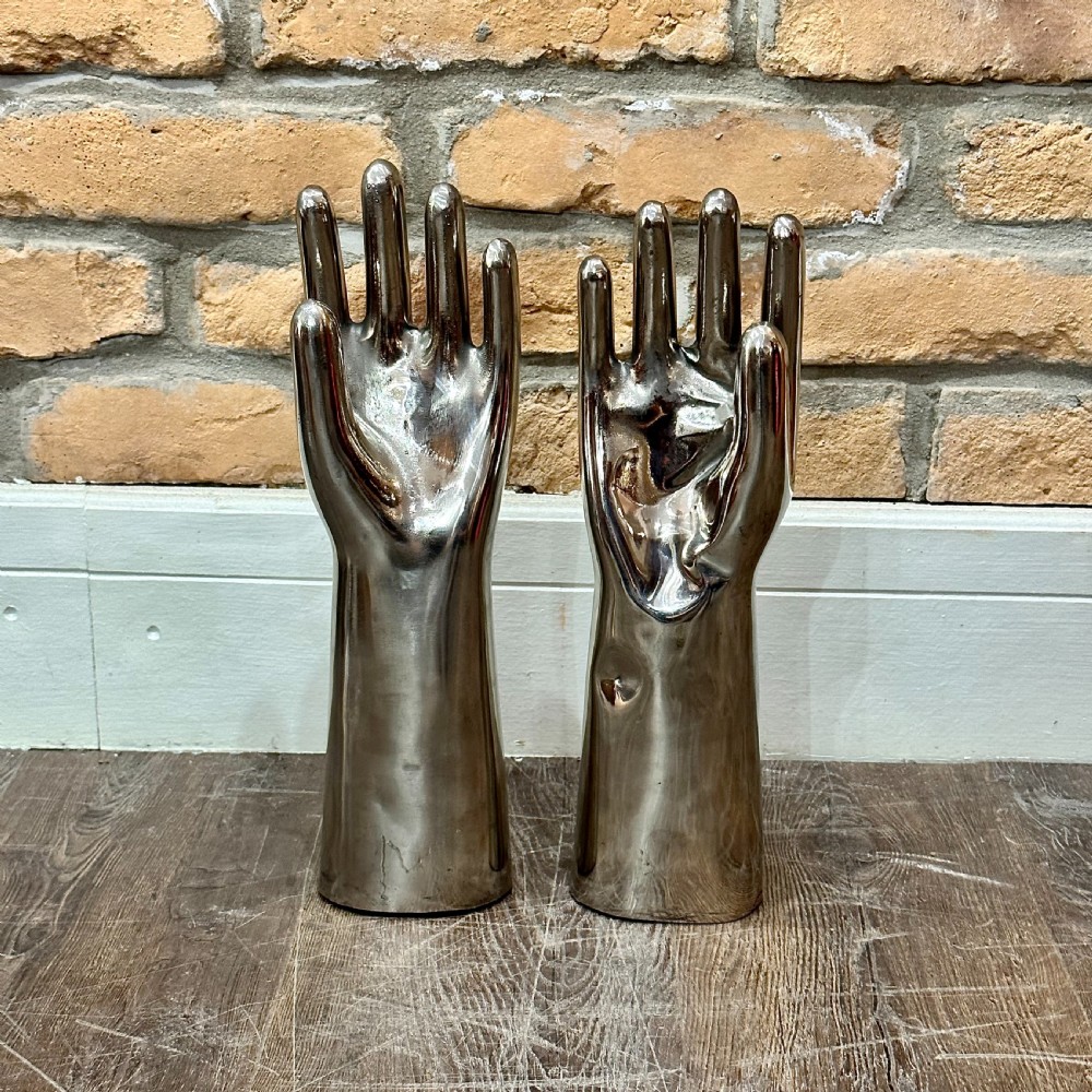 A pair of polished silver aluminium hand-shaped glove moulds standing vertically on flat bases.