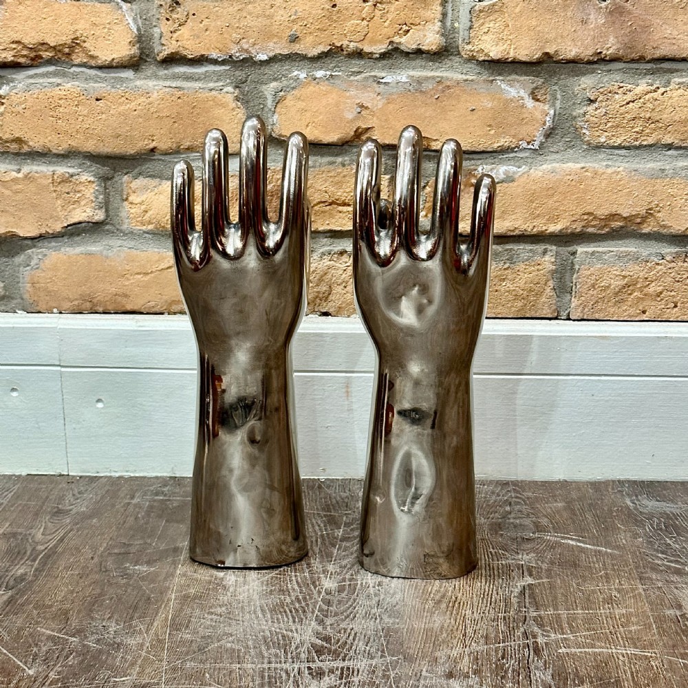 A pair of polished silver aluminium hand-shaped glove moulds standing vertically on flat bases. View II