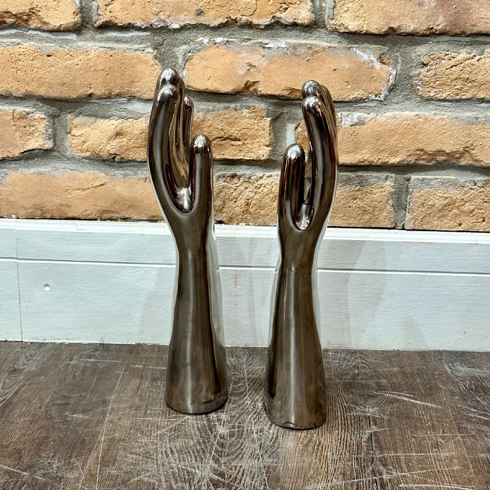 A pair of polished silver aluminium hand-shaped glove moulds standing vertically on flat bases. View III