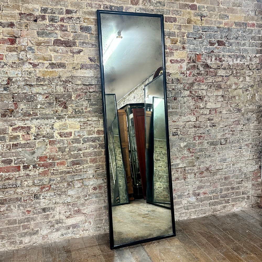A tall rectangular full-length floor mirror with a slender black timber frame and foxed mercury glass plate.