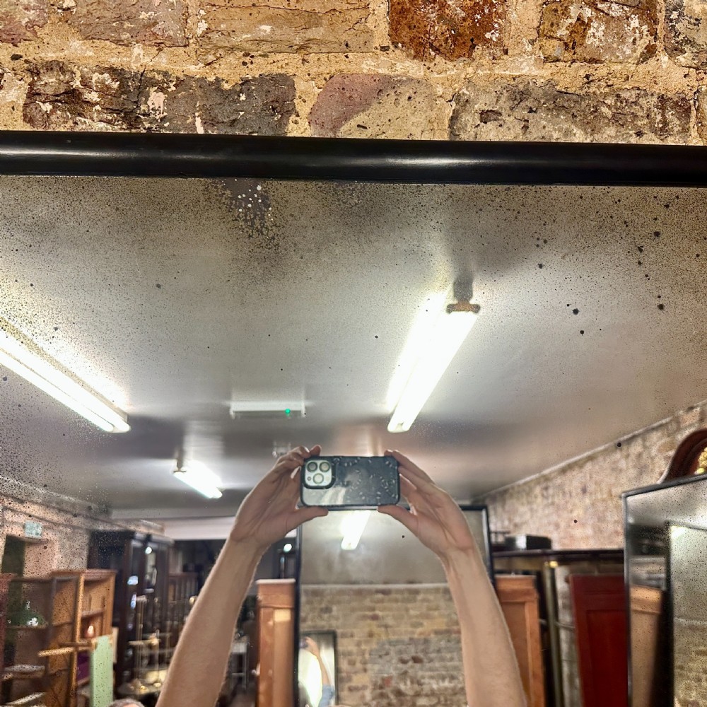 A tall rectangular full-length floor mirror with a slender black timber frame and foxed mercury glass plate. View V