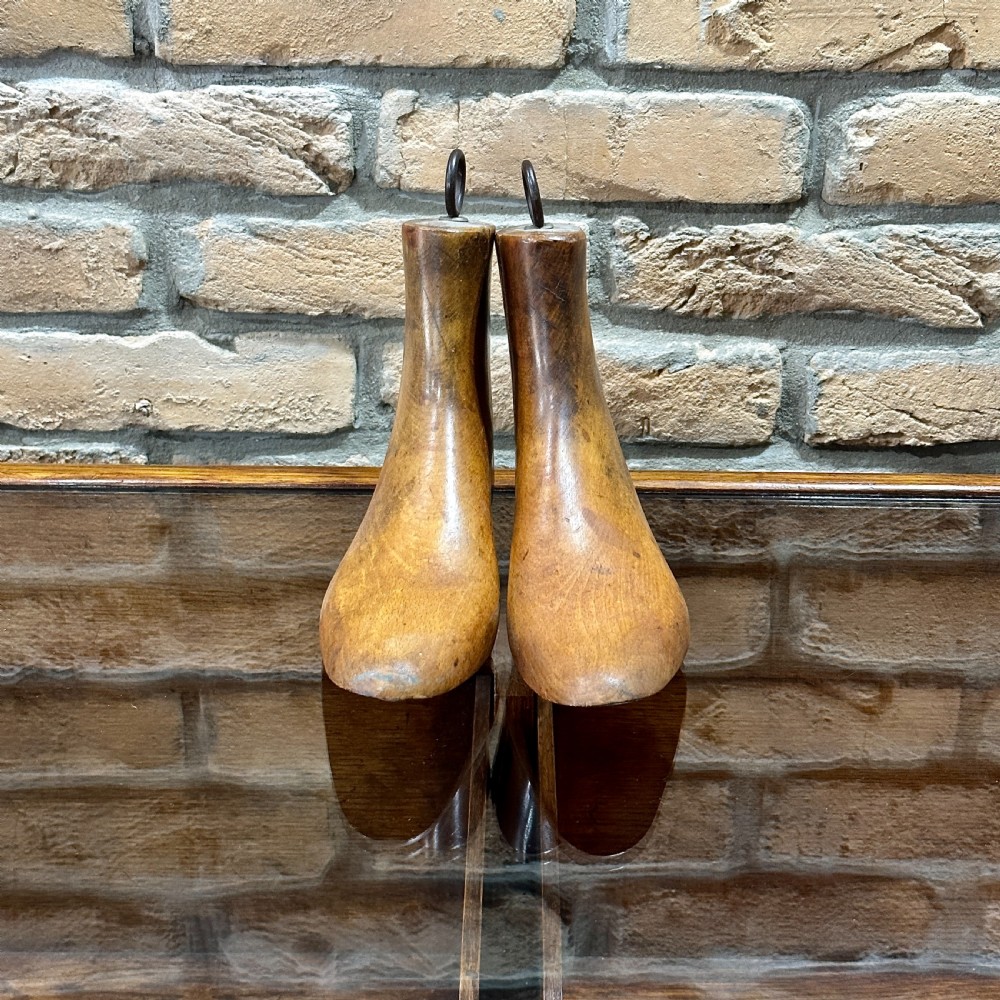 A pair of carved wooden boot trees with iron ring pull handles standing side by side.