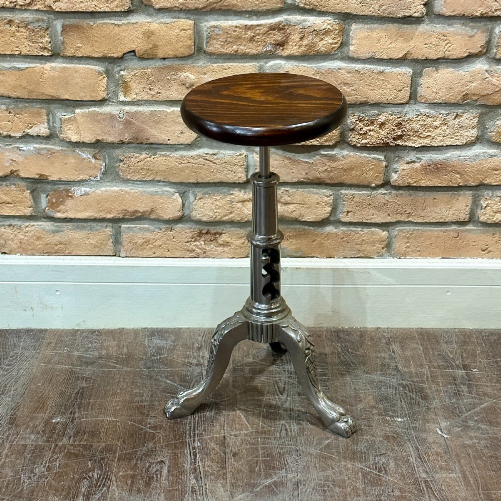 A Victorian industrial style height-adjustable stool featuring a dark round wooden seat resting on a silver-coloured cast metal tripod stem with ornate claw feet.
