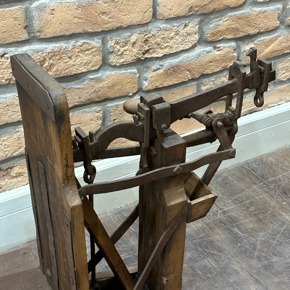 An antique floor platform scale featuring a wooden base, metal platform, and an exposed cast iron mechanical weighing arm. View II