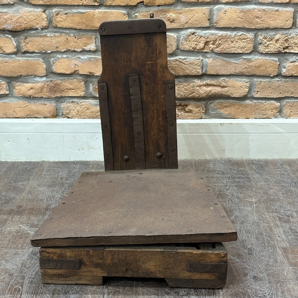 An antique floor platform scale featuring a wooden base, metal platform, and an exposed cast iron mechanical weighing arm. View III