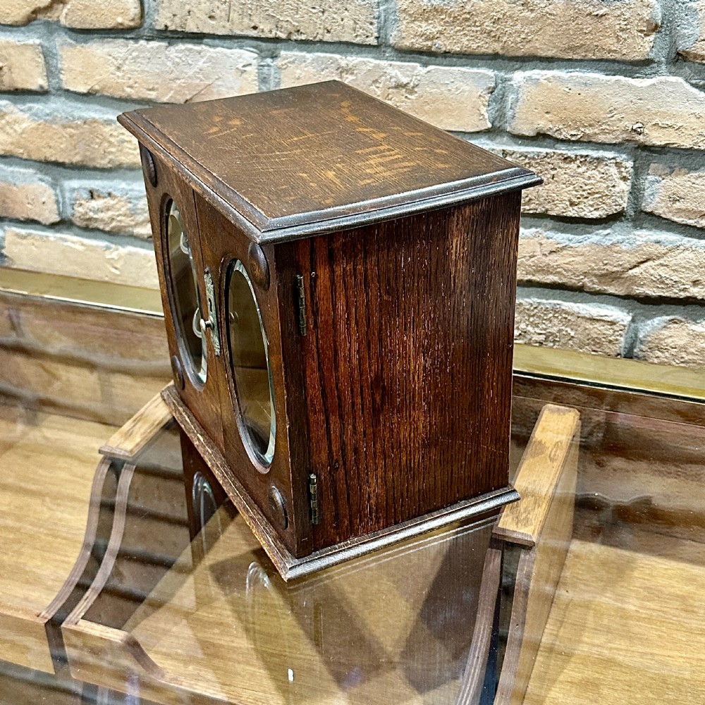 An Edwardian dark oak desktop smokers cabinet featuring twin doors with oval glass aperture windows and brass fittings. View VI