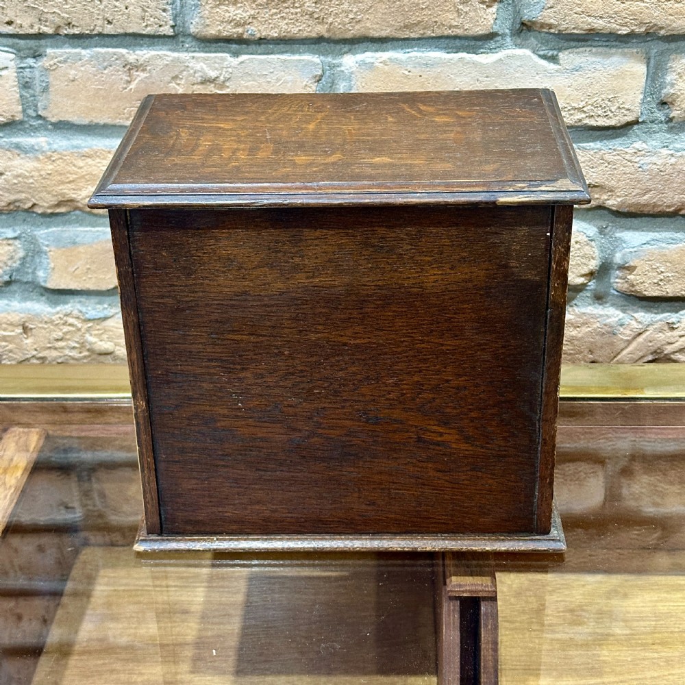 An Edwardian dark oak desktop smokers cabinet featuring twin doors with oval glass aperture windows and brass fittings. View VII