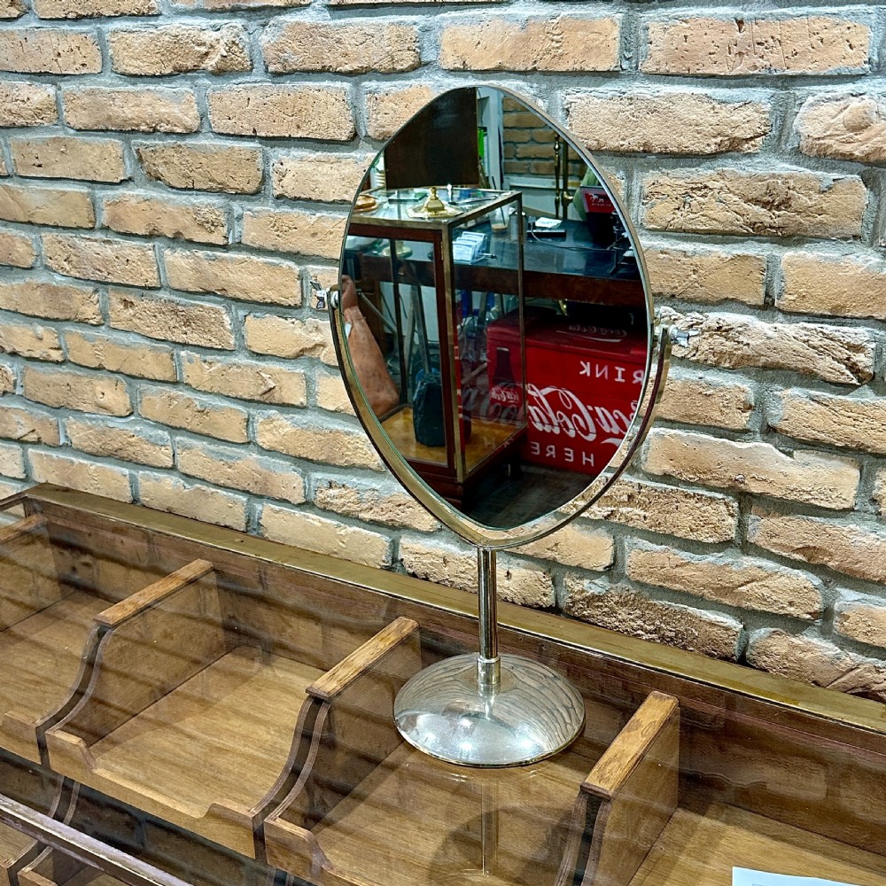 An Art Deco chrome vanity mirror featuring an oval glass frame supported by a central pedestal and circular dome base.