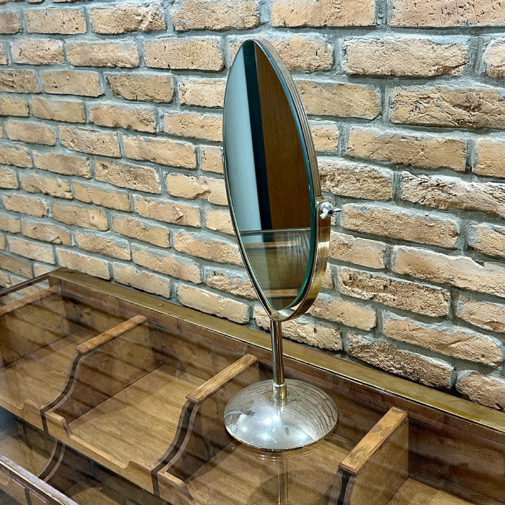 An Art Deco chrome vanity mirror featuring an oval glass frame supported by a central pedestal and circular dome base. View IV