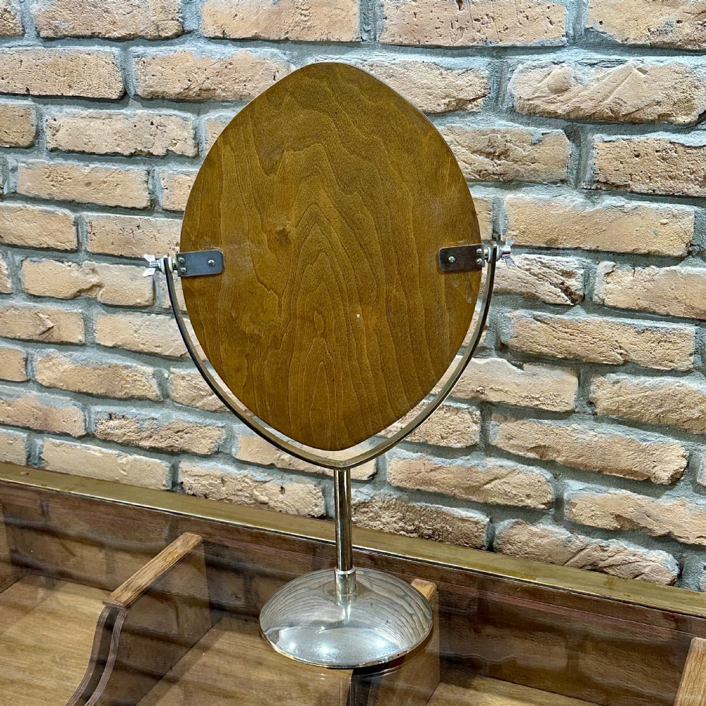 An Art Deco chrome vanity mirror featuring an oval glass frame supported by a central pedestal and circular dome base. View V
