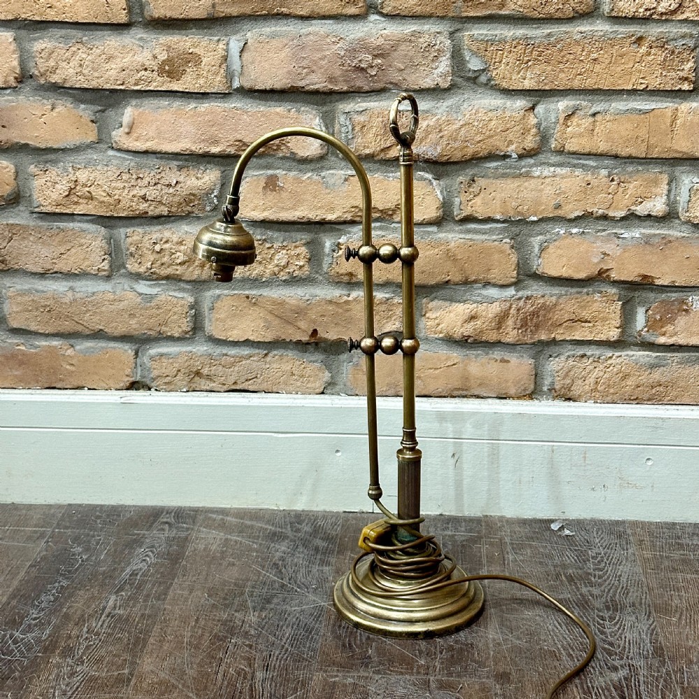 A vintage brass swan neck desk lamp featuring an adjustable curved arm, stepped circular base, and turned fitting details.
