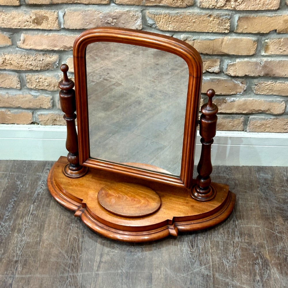 A Victorian mahogany swivel toilet mirror with turned side columns and a sculpted plinth base featuring an oval tray.