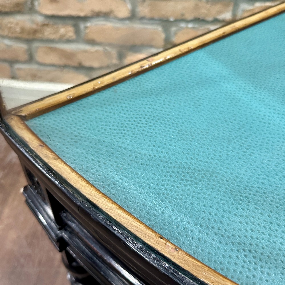 A 1920s quadrant-shaped ebonised shop display counter featuring all-around clear glass panels, turned legs, and a teal fabric-lined base. View V