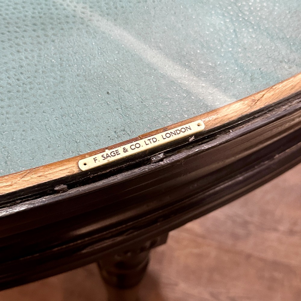 A 1920s quadrant-shaped ebonised shop display counter featuring all-around clear glass panels, turned legs, and a teal fabric-lined base. View VIII
