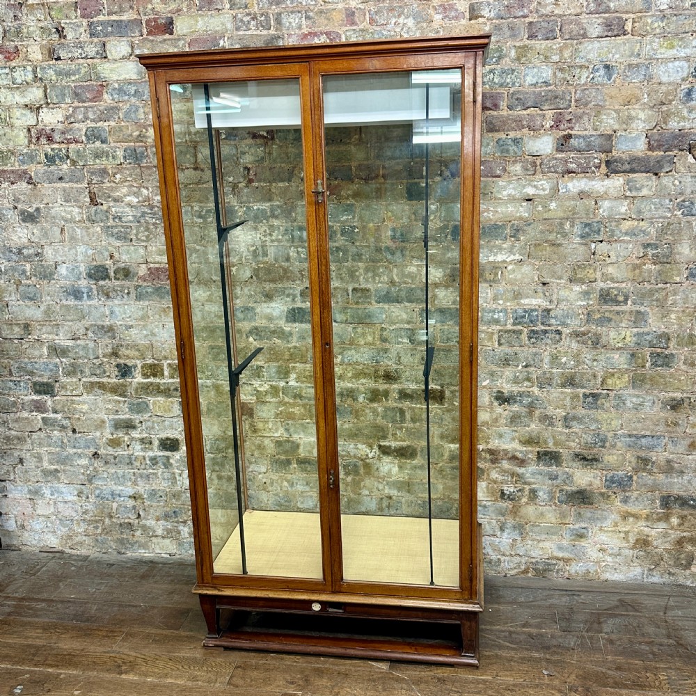A tall glazed mahogany shop display cabinet featuring double glass doors, side glass panels, and internal metal shelf brackets on a plinth base.