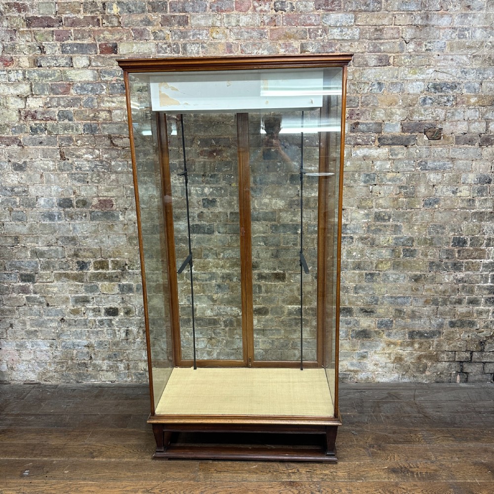 A tall glazed mahogany shop display cabinet featuring double glass doors, side glass panels, and internal metal shelf brackets on a plinth base. View III