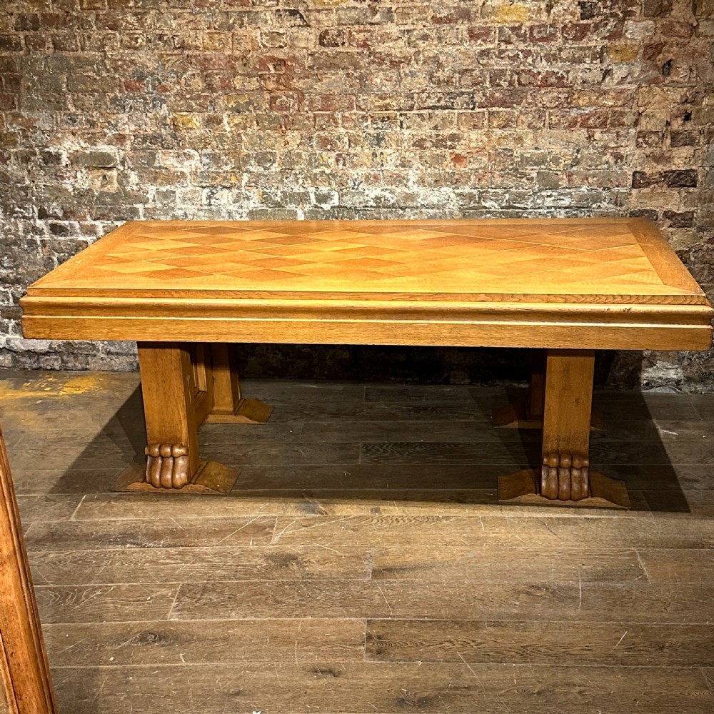 A large rectangular French Art Deco dining table featuring a geometric parquetry top and sturdy carved supports.