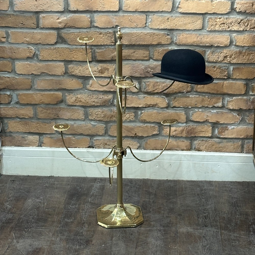 A polished brass multi-arm countertop hat stand featuring a reeded central column, six curved display arms, and a weighted octagonal base.