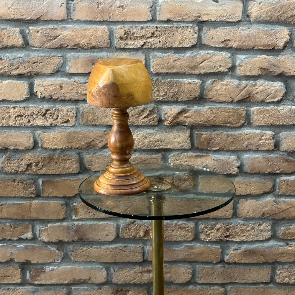 A solid turned beechwood hat block mounted on a turned pedestal and circular stepped base.