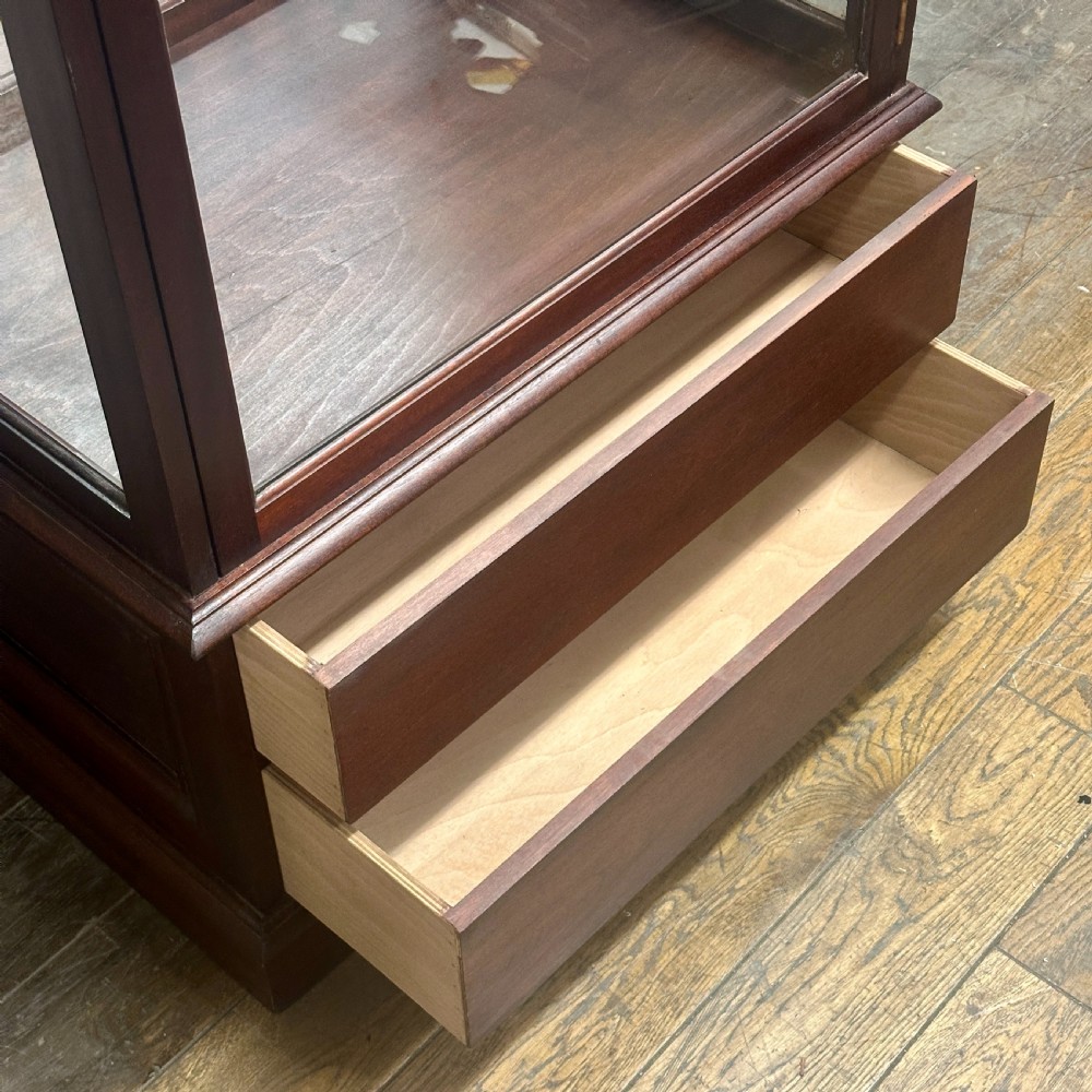 A tall 1920s mahogany shop display cabinet featuring full-length glass side panels, a glazed front door, internal shelf supports, and a solid timber plinth base. View II