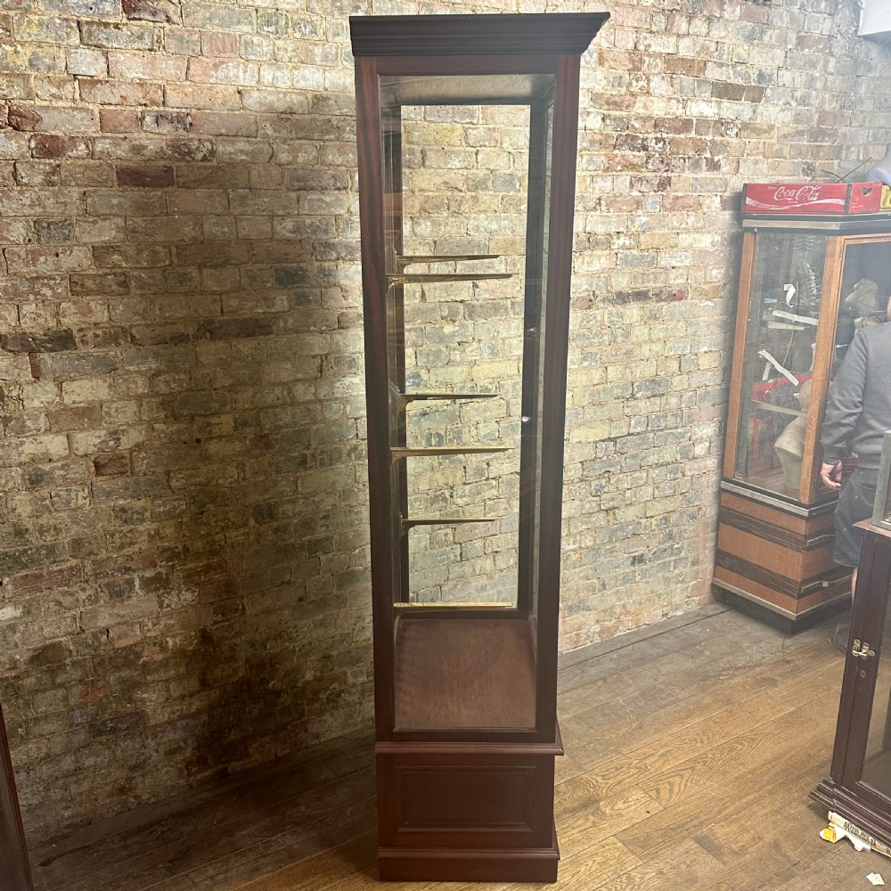 A tall 1920s mahogany shop display cabinet featuring full-length glass side panels, a glazed front door, internal shelf supports, and a solid timber plinth base. View V