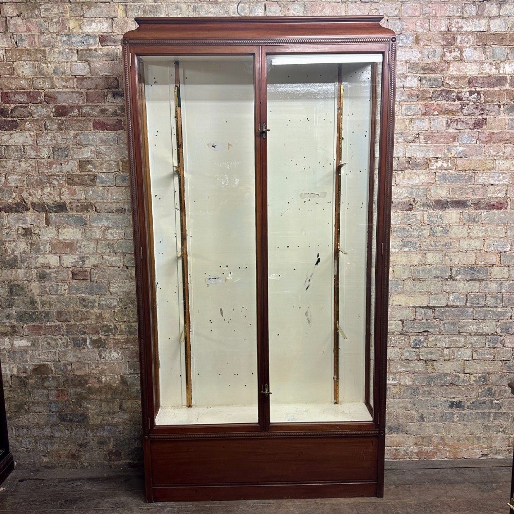 A tall dark mahogany glazed shop display cabinet featuring two full-length glass doors and internal brass ratchet supports.