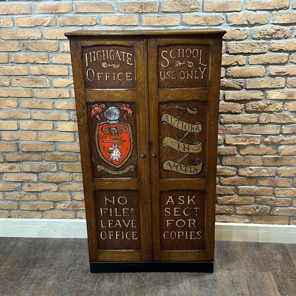 A vintage 1930s oak school cabinet featuring two doors with hand-painted institutional lettering and a crest.