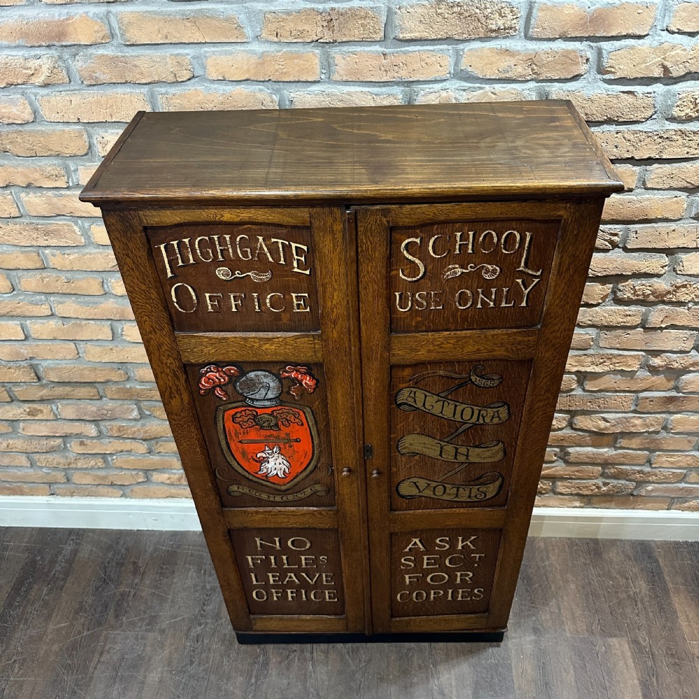 A vintage 1930s oak school cabinet featuring two doors with hand-painted institutional lettering and a crest. View III