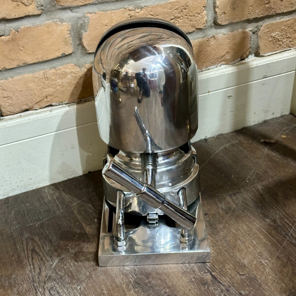 A restored 1930s polished aluminium mechanical hat stretcher with a turn handle set on a solid metal base.