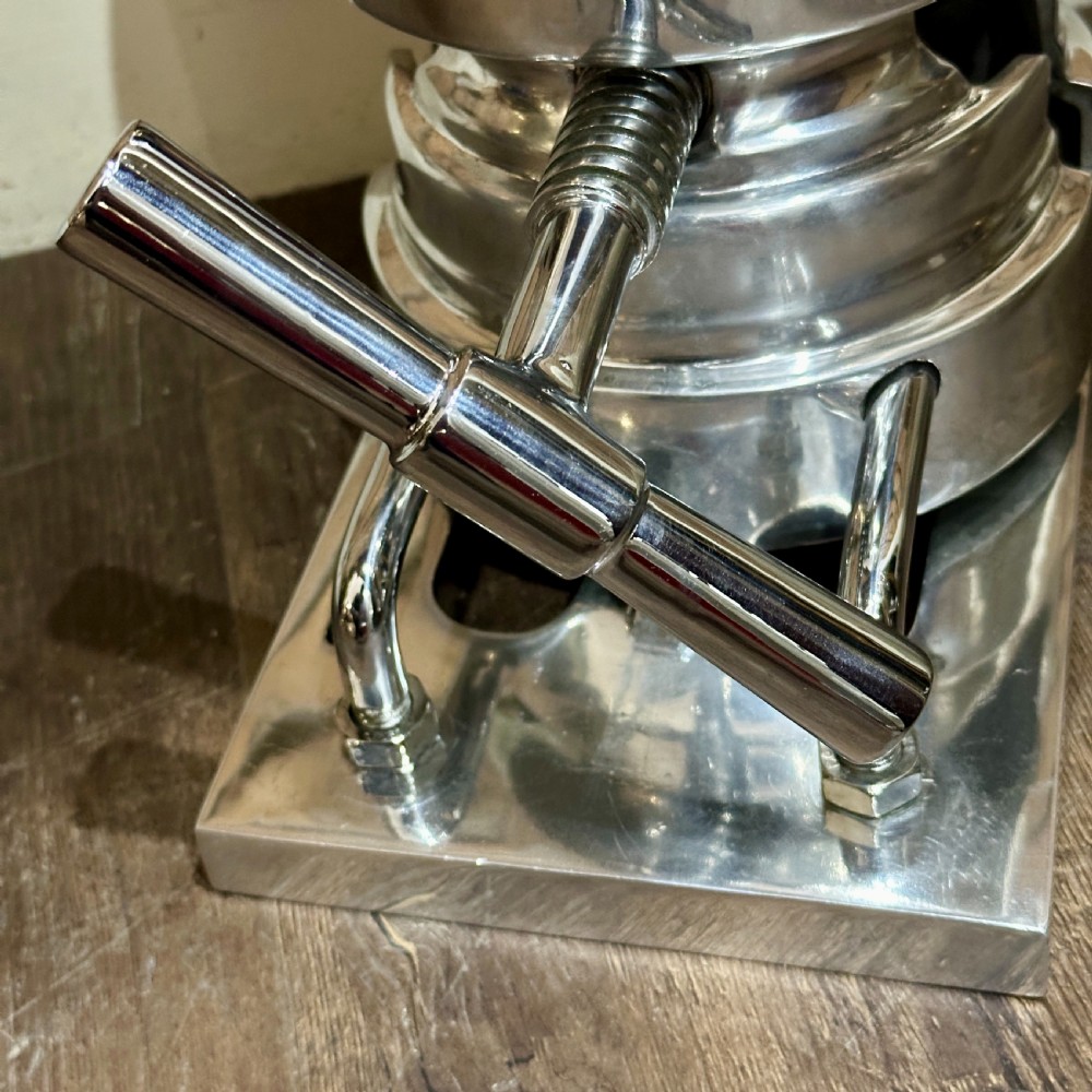 A restored 1930s polished aluminium mechanical hat stretcher with a turn handle set on a solid metal base. View II