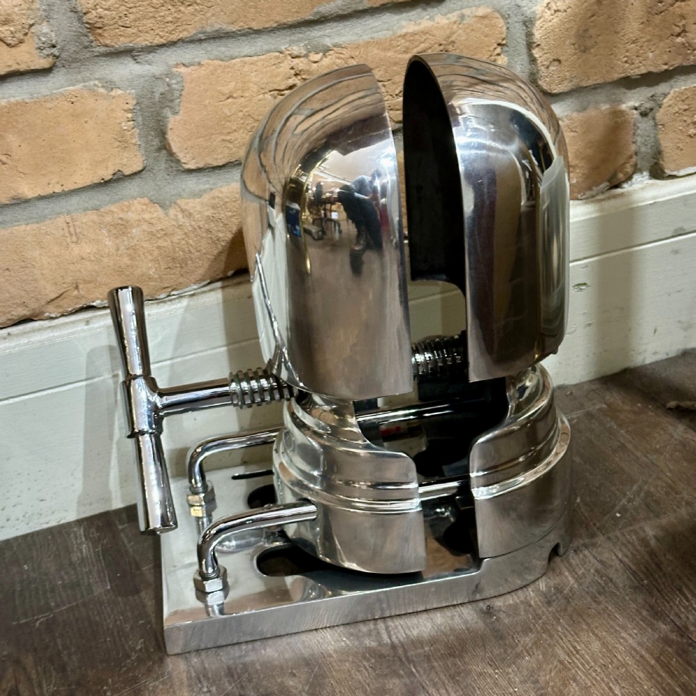 A restored 1930s polished aluminium mechanical hat stretcher with a turn handle set on a solid metal base. View III