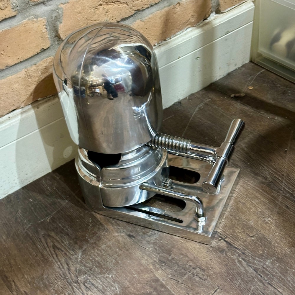 A restored 1930s polished aluminium mechanical hat stretcher with a turn handle set on a solid metal base. View VI