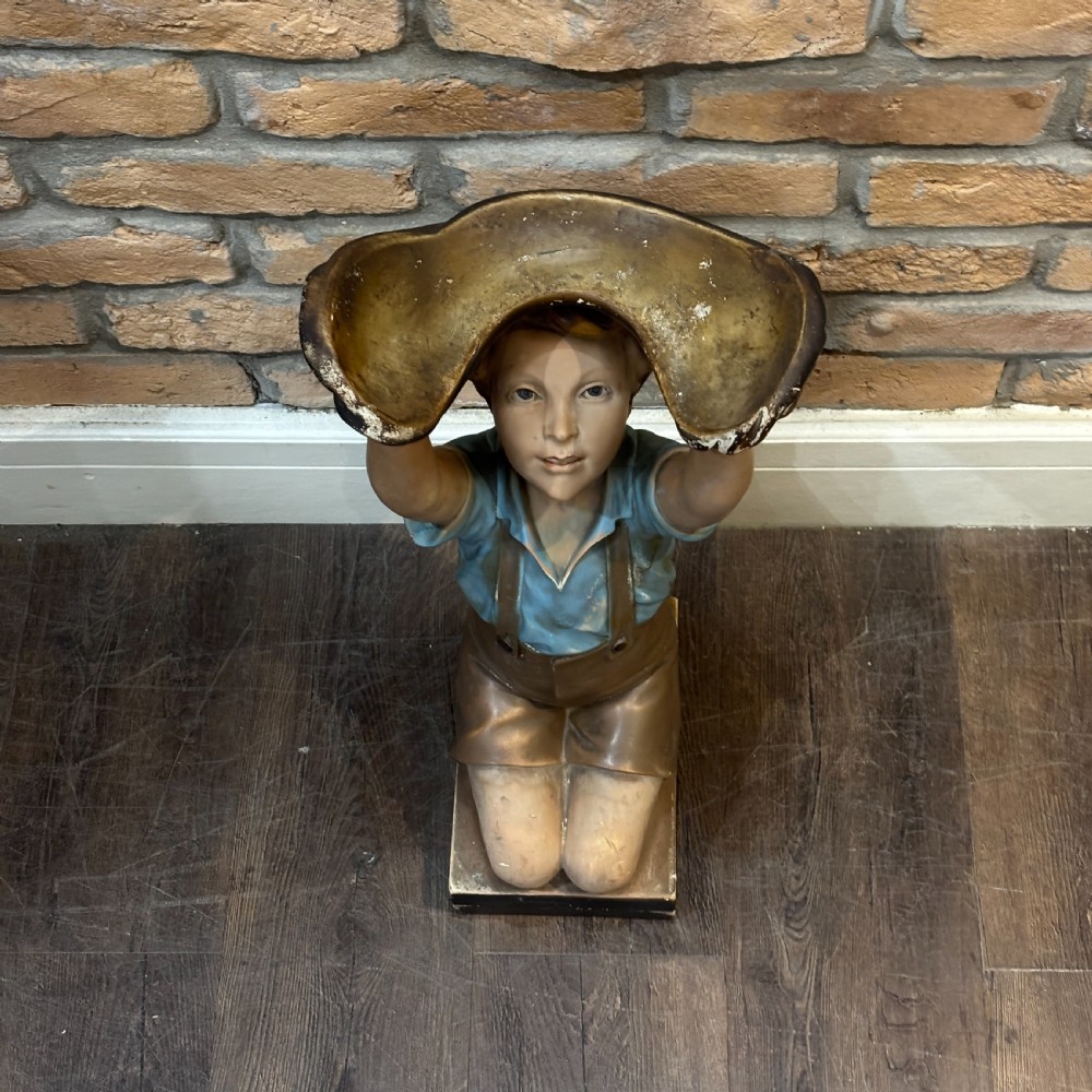 A hand-painted 1920s plaster sculpture of a kneeling boy wearing a blue shirt and brown shorts, supporting a shell-shaped tray overhead. View II
