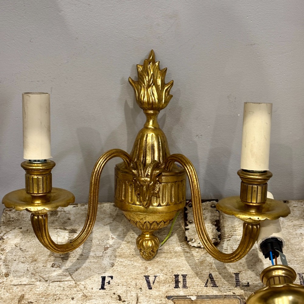 A pair of antique gilt bronze two-arm wall sconces featuring neoclassical urn motifs, reeded branches, and cream candle sleeves. View II