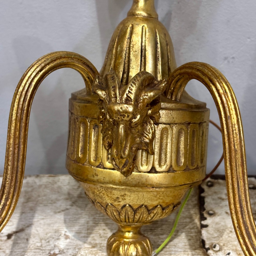 A pair of antique gilt bronze two-arm wall sconces featuring neoclassical urn motifs, reeded branches, and cream candle sleeves. View IV