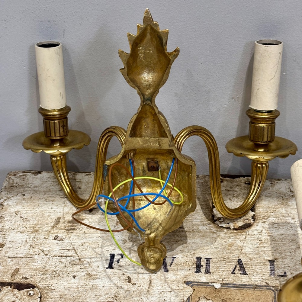 A pair of antique gilt bronze two-arm wall sconces featuring neoclassical urn motifs, reeded branches, and cream candle sleeves. View VI