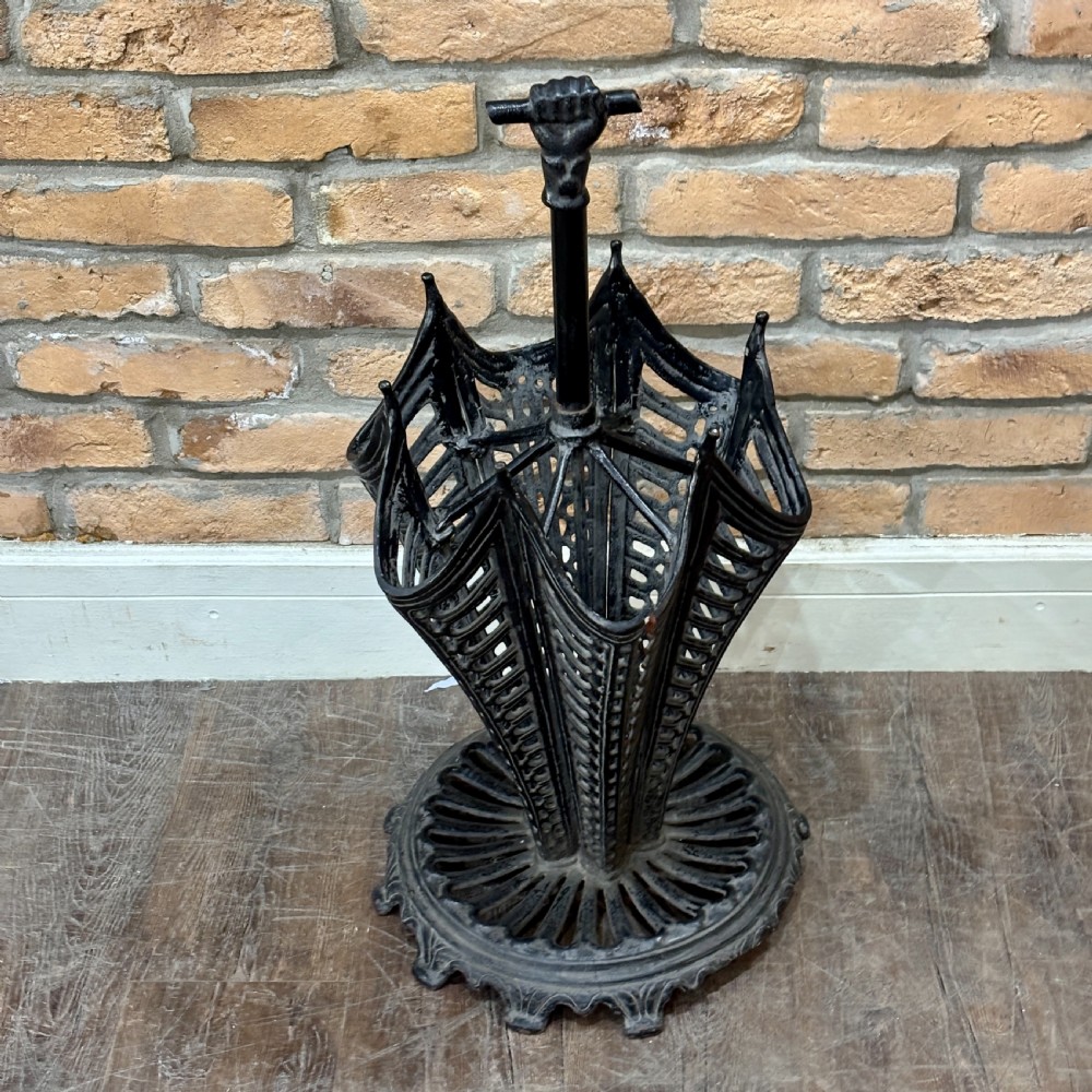 A black cast iron umbrella stand shaped like a folded umbrella with a central shaft ending in a fist handle, set on a circular fluted base.