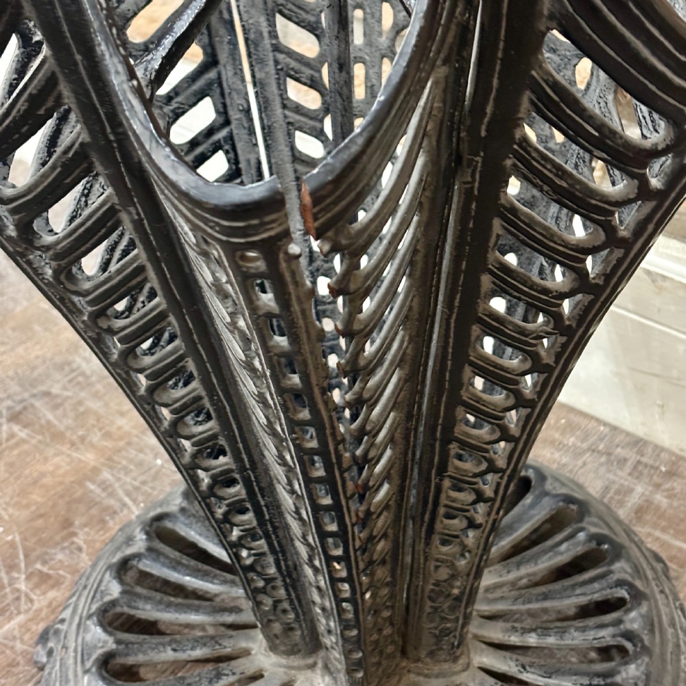 A black cast iron umbrella stand shaped like a folded umbrella with a central shaft ending in a fist handle, set on a circular fluted base. View III