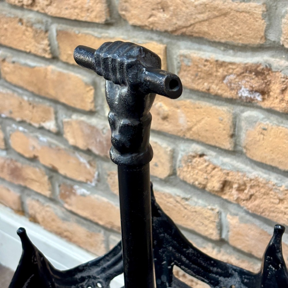 A black cast iron umbrella stand shaped like a folded umbrella with a central shaft ending in a fist handle, set on a circular fluted base. View IV