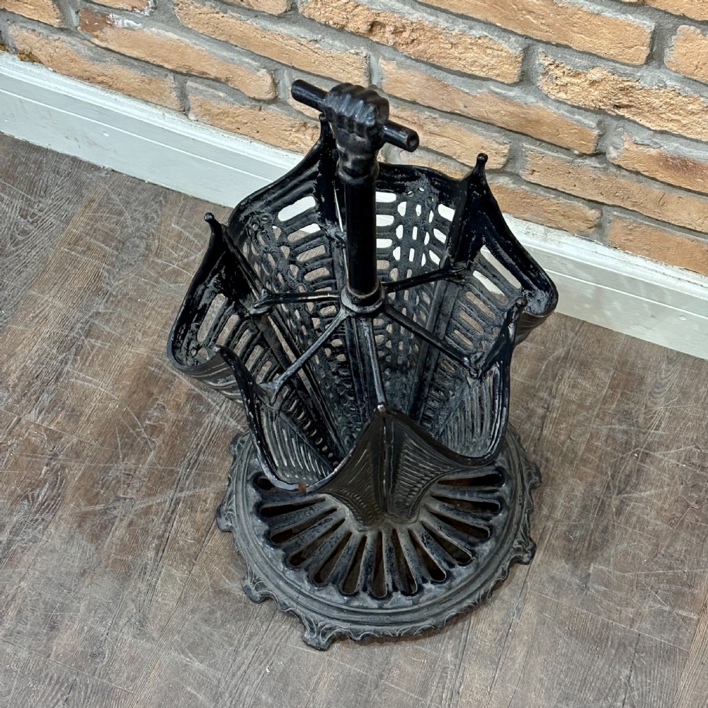 A black cast iron umbrella stand shaped like a folded umbrella with a central shaft ending in a fist handle, set on a circular fluted base. View V