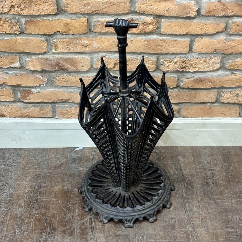 A black cast iron umbrella stand shaped like a folded umbrella with a central shaft ending in a fist handle, set on a circular fluted base. View VI